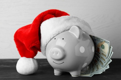 Piggy bank with Santa hat and dollar banknotes on black wooden table