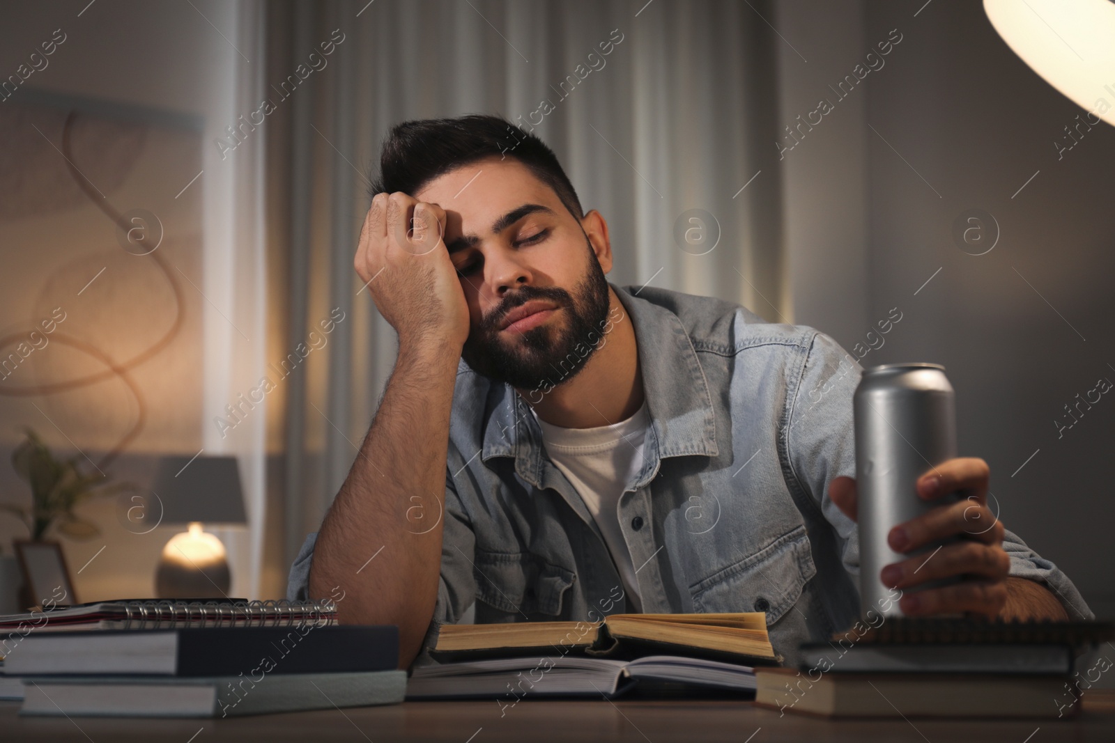 Photo of Tired young man with energy drink studying at home