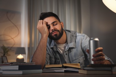Photo of Tired young man with energy drink studying at home