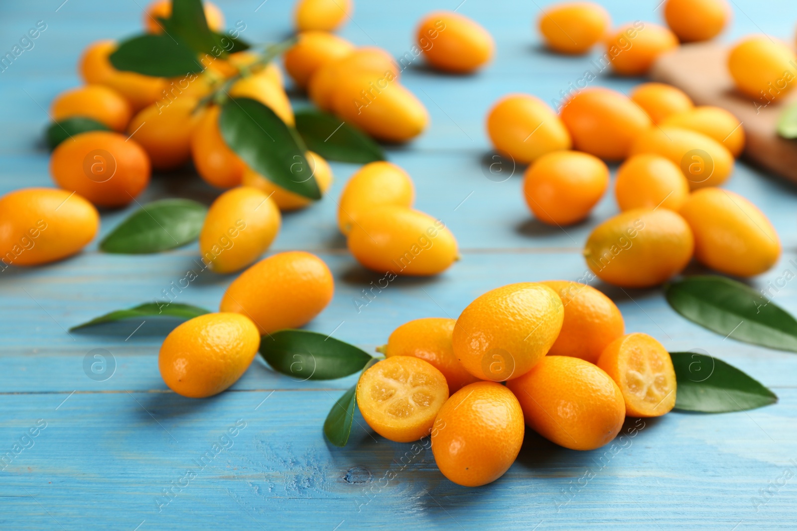 Photo of Fresh ripe kumquats and leaves on light blue wooden table