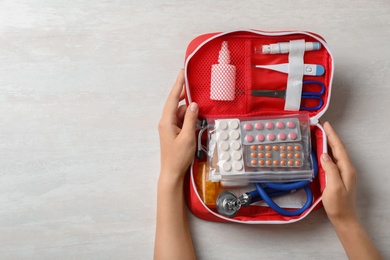 Photo of Woman holding first aid kit on white wooden table, top view. Space for text