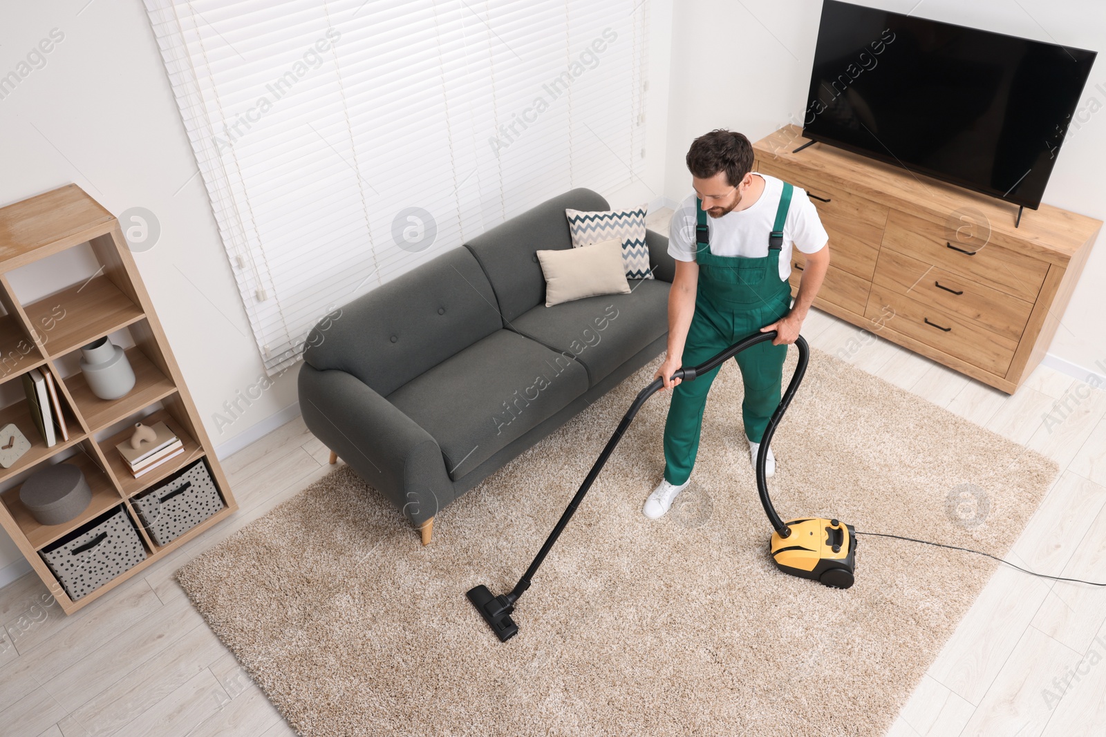 Photo of Dry cleaner's employee hoovering carpet with vacuum cleaner in room, above view