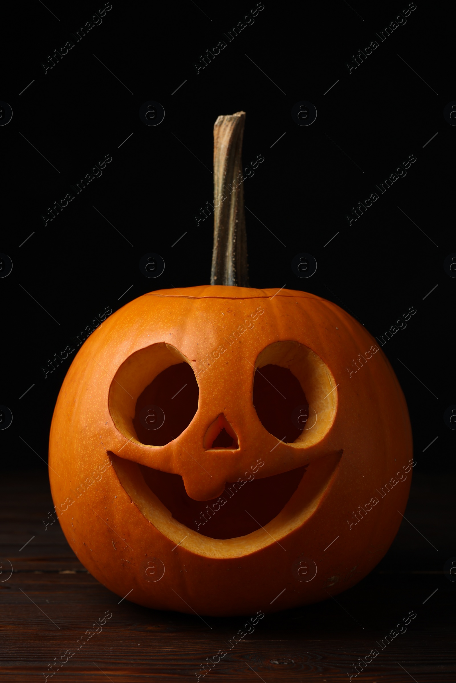 Photo of Scary jack o'lantern made of pumpkin on wooden table in darkness. Halloween traditional decor