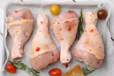 Photo of Raw marinated chicken drumsticks, rosemary and tomatoes in baking dish on table, top view