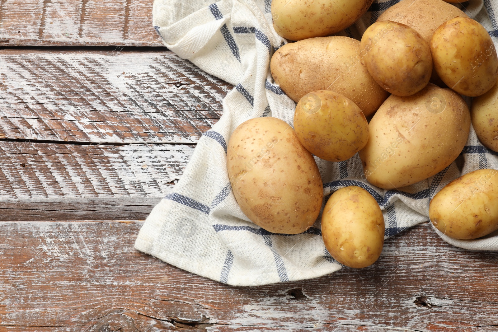 Photo of Raw fresh potatoes and napkin on wooden table, top view. Space for text