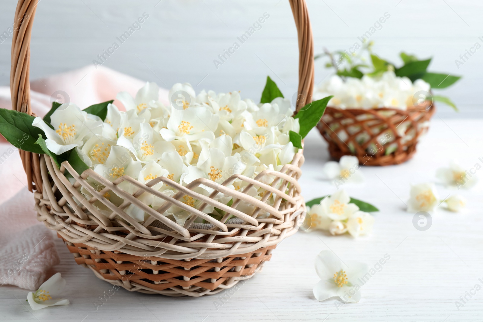 Photo of Beautiful jasmine flowers in wicker basket on white wooden table