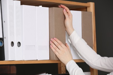 Woman taking folder with documents from shelf in office, closeup