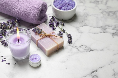 Cosmetic products and lavender flowers on white marble table. Space for text