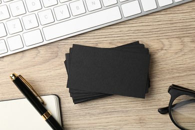 Photo of Blank black business cards, computer keyboard and stationery on wooden table, flat lay. Mockup for design