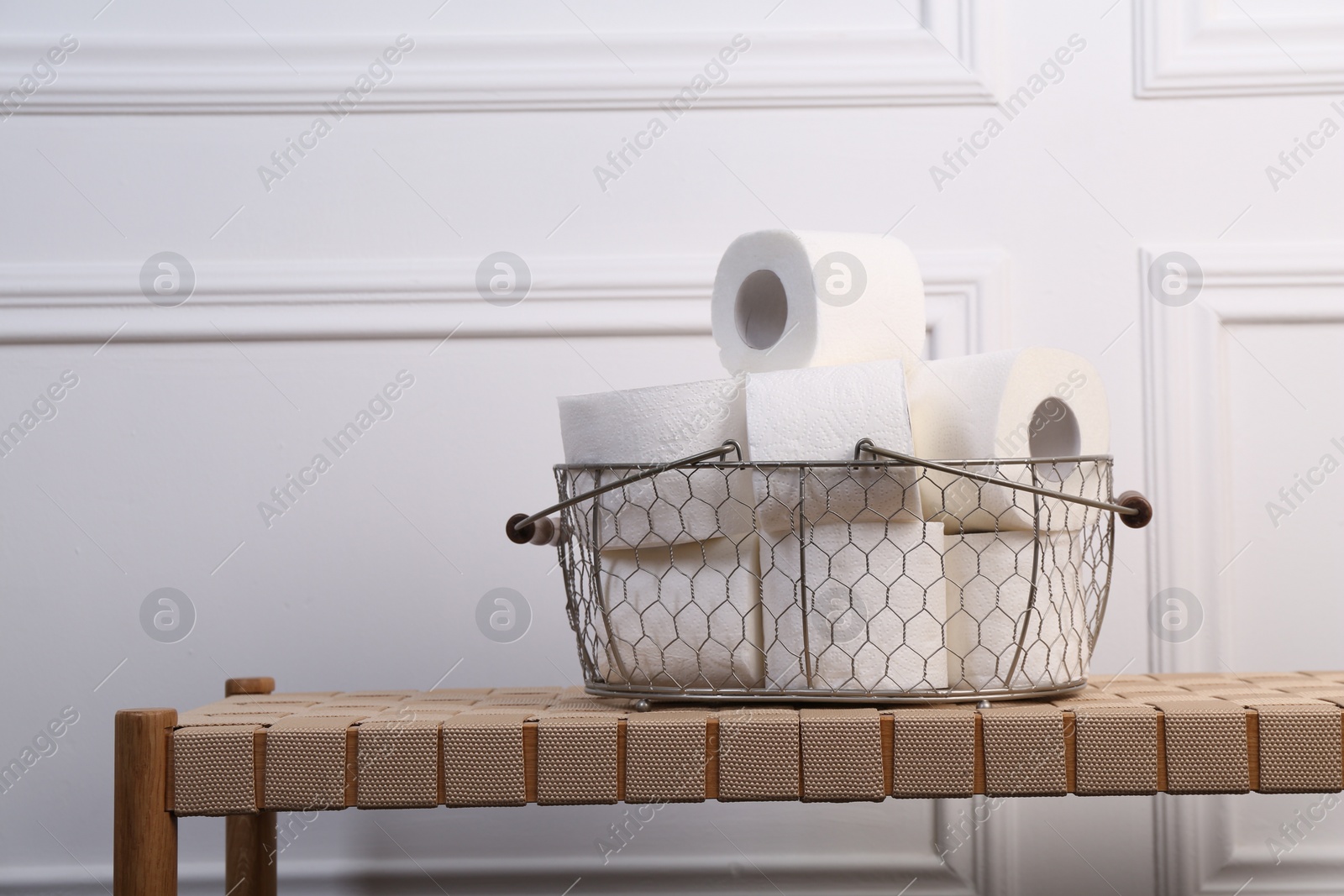 Photo of Soft toilet paper rolls in metal basket on wicker bench. Space for text