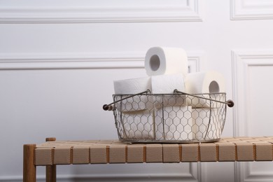 Photo of Soft toilet paper rolls in metal basket on wicker bench. Space for text