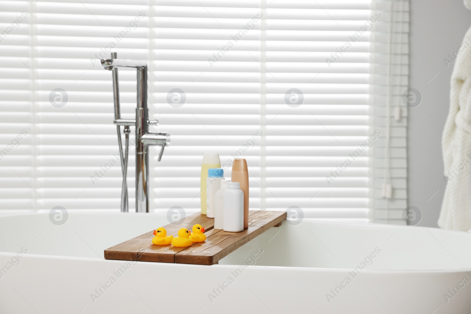 Photo of Wooden tray with toys and personal care products on tub in bathroom. Interior design