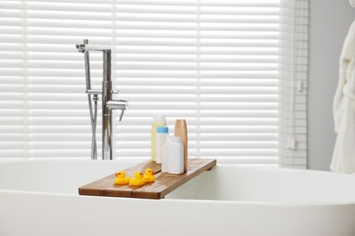 Wooden tray with toys and personal care products on tub in bathroom. Interior design