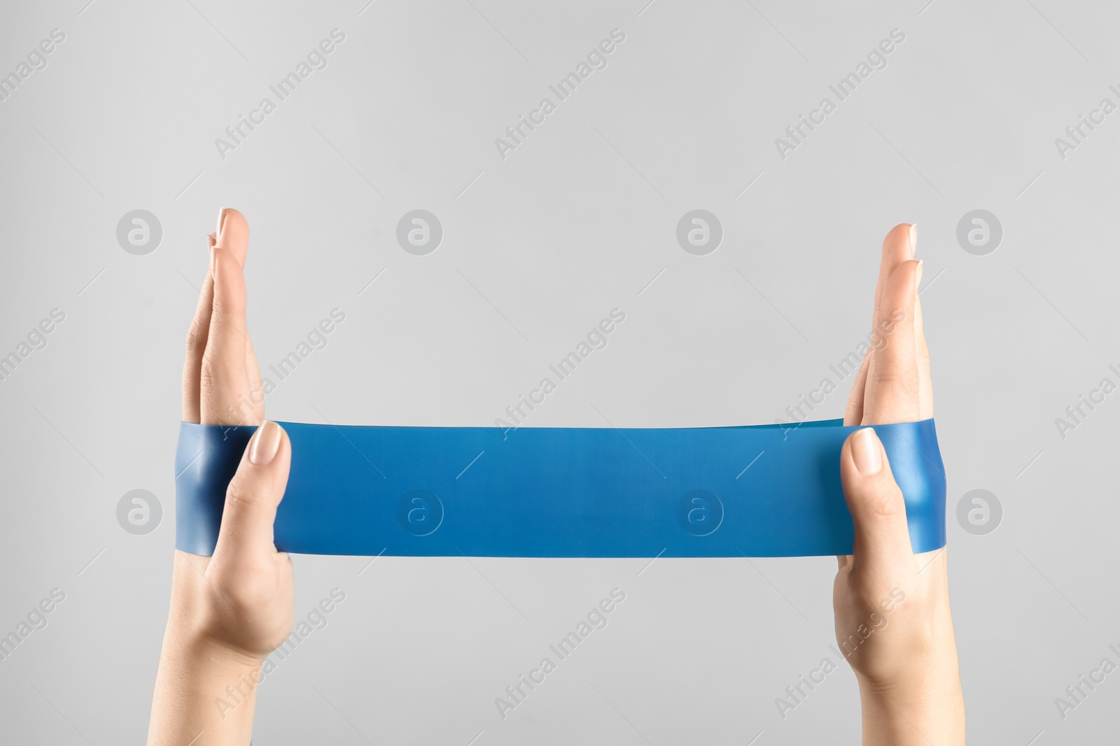 Photo of Woman with fitness elastic band on light grey background, closeup