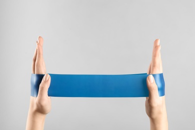 Photo of Woman with fitness elastic band on light grey background, closeup