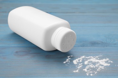Bottle and scattered baby powder on light blue wooden table, closeup