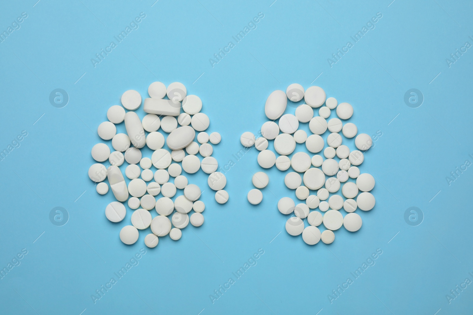 Photo of White pills in shape of kidneys on light blue background, flat lay