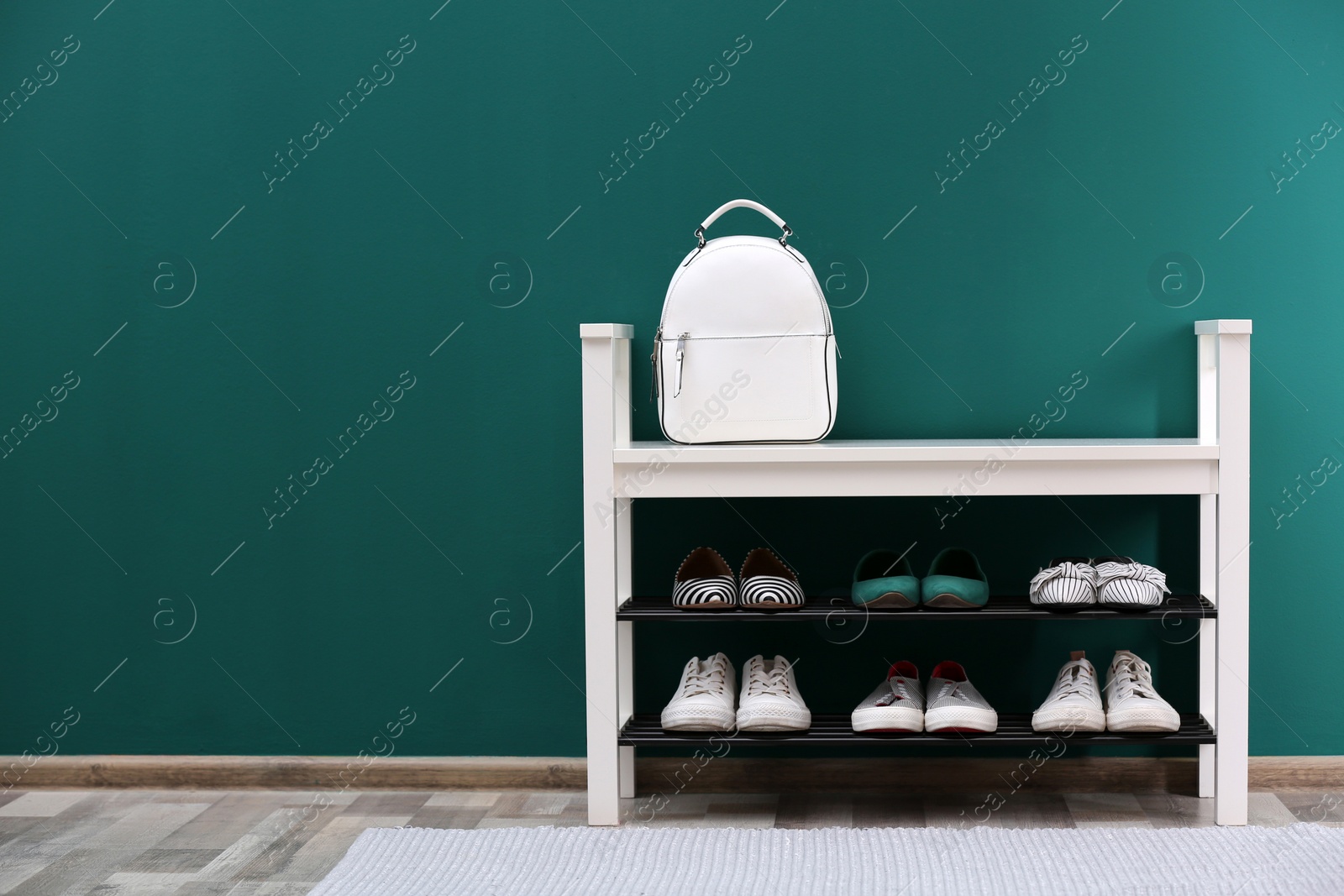 Photo of Shoe rack with different footwear near color wall, space for text. Stylish hallway interior