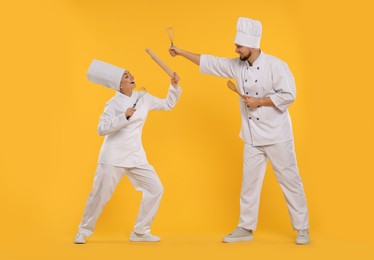 Photo of Happy professional confectioners in uniforms having fun on yellow background