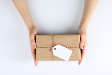 Photo of Woman holding parcel wrapped in kraft paper with tag on white background, top view