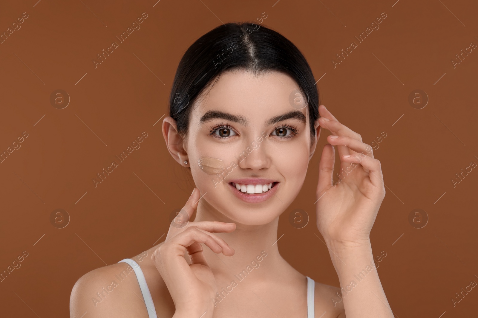 Photo of Teenage girl with swatch of foundation on face against brown background