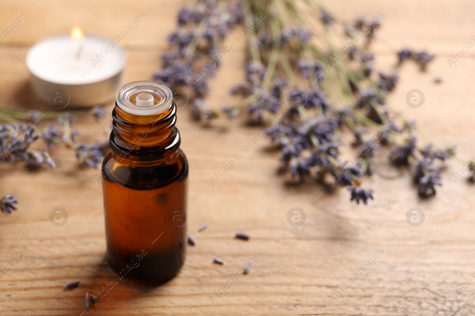 Photo of Bottle of essential oil and lavender flowers on wooden table, space for text