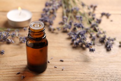 Bottle of essential oil and lavender flowers on wooden table, space for text