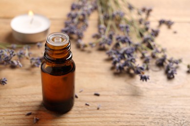 Photo of Bottle of essential oil and lavender flowers on wooden table, space for text