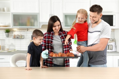 Happy family with tray of oven baked buns in kitchen