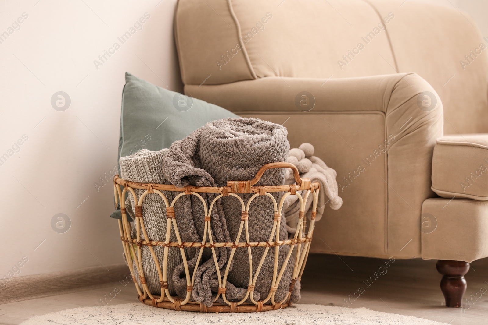 Photo of Wicker basket with rolled blankets and pillow near beige sofa. Idea for interior design