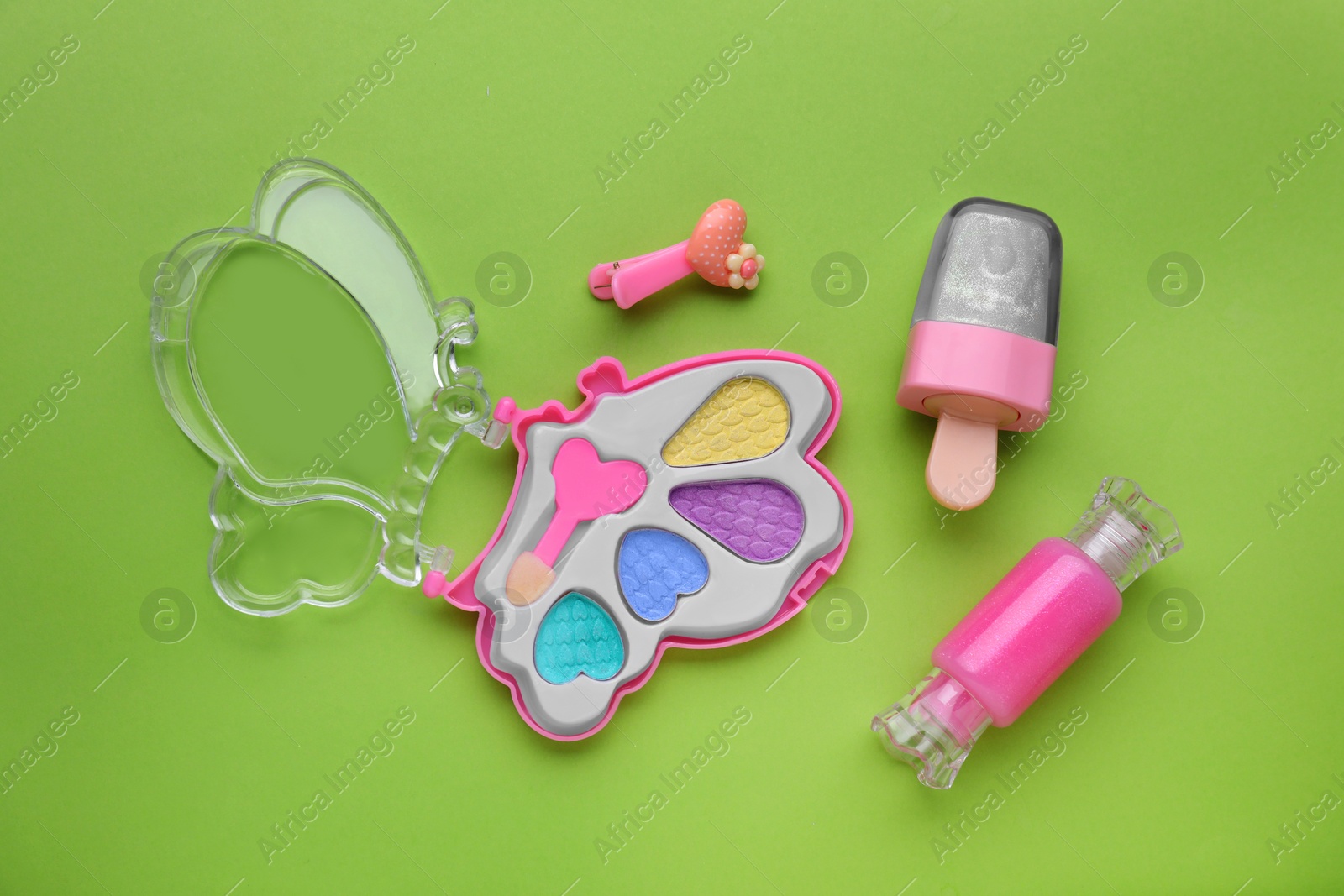 Photo of Decorative cosmetics for kids. Eye shadow palette, lip glosses and hairpin on light green background, flat lay