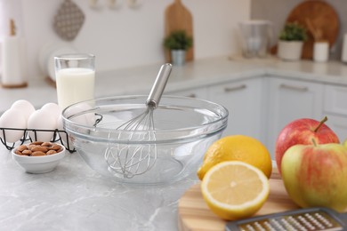 Photo of Metal whisk, bowl and different products on gray marble table in kitchen