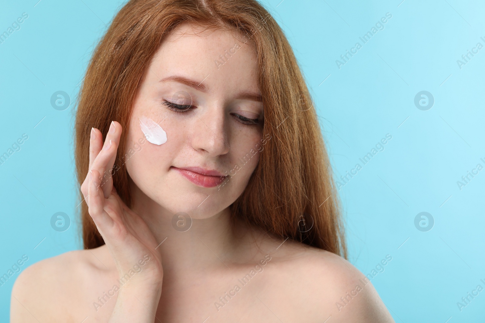 Photo of Beautiful woman with freckles and cream on her face against light blue background