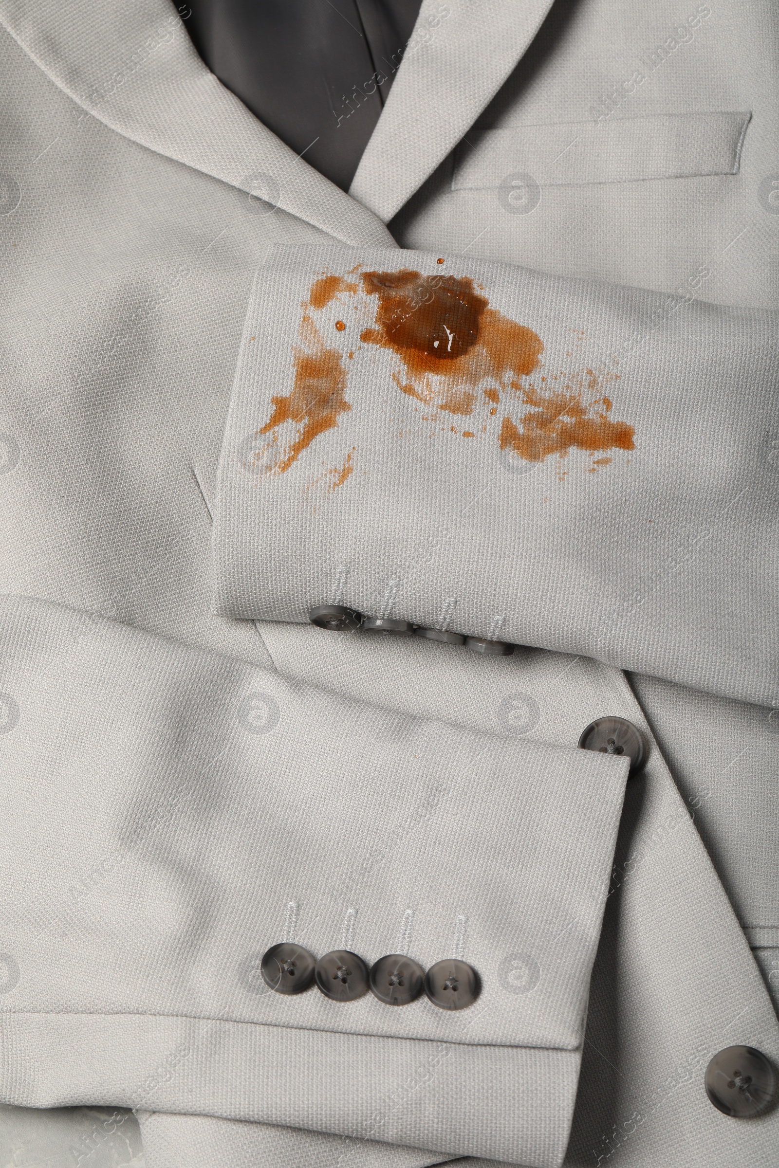 Photo of Dirty jacket with stain of coffee on light grey surface, top view