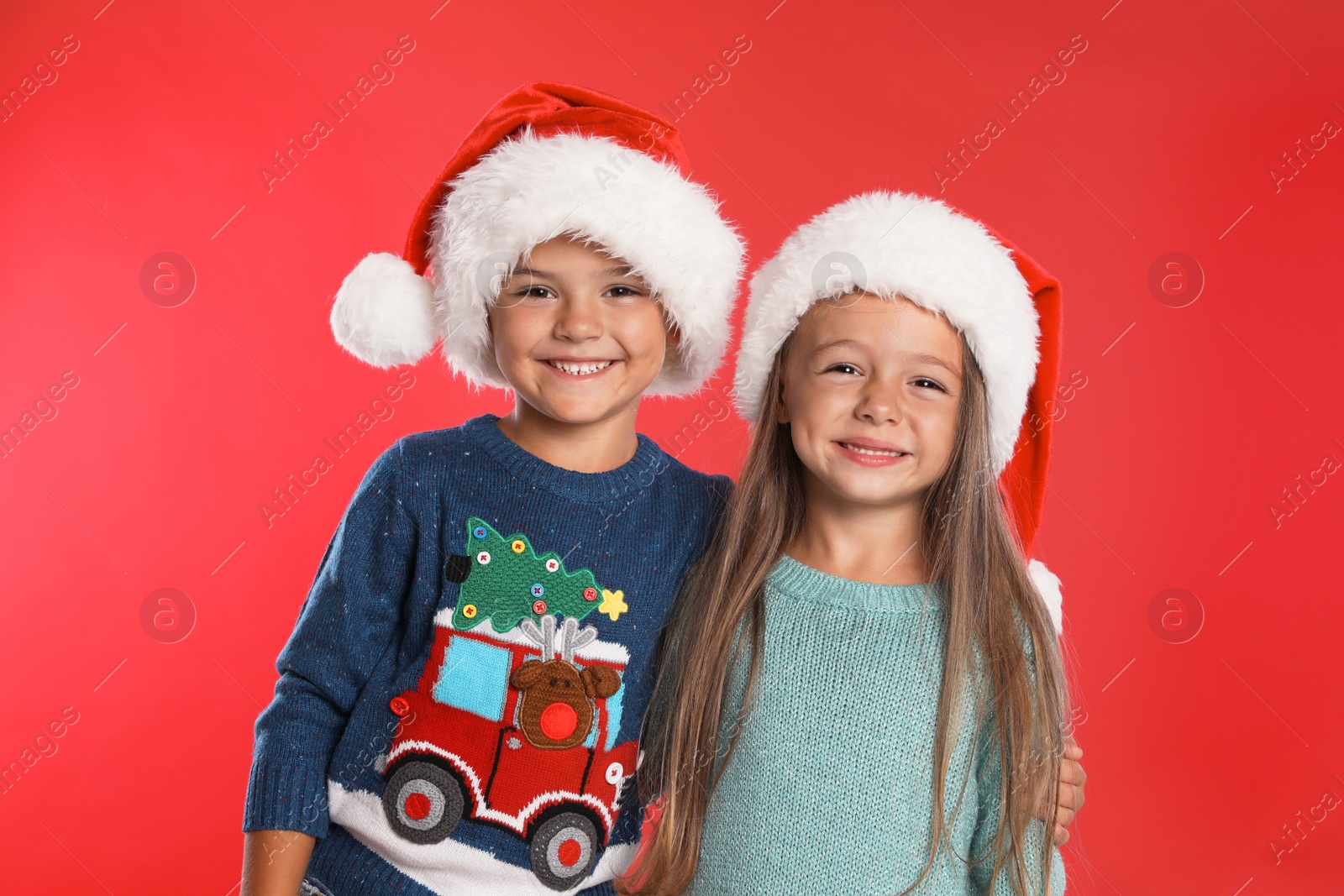 Photo of Happy little children in Santa hats on red background. Christmas celebration