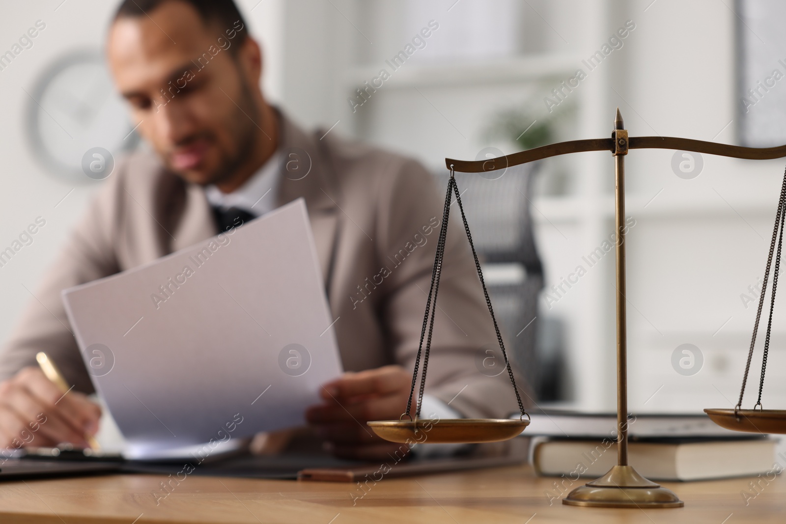 Photo of Lawyer working with document at table in office, focus on scales of justice