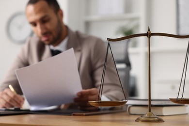 Lawyer working with document at table in office, focus on scales of justice