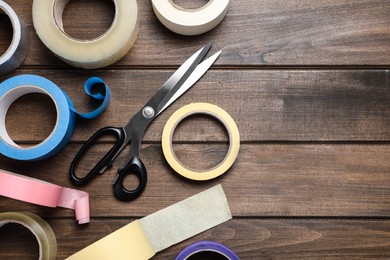 Photo of Rolls of adhesive tape and scissors on wooden background, flat lay. Space for text