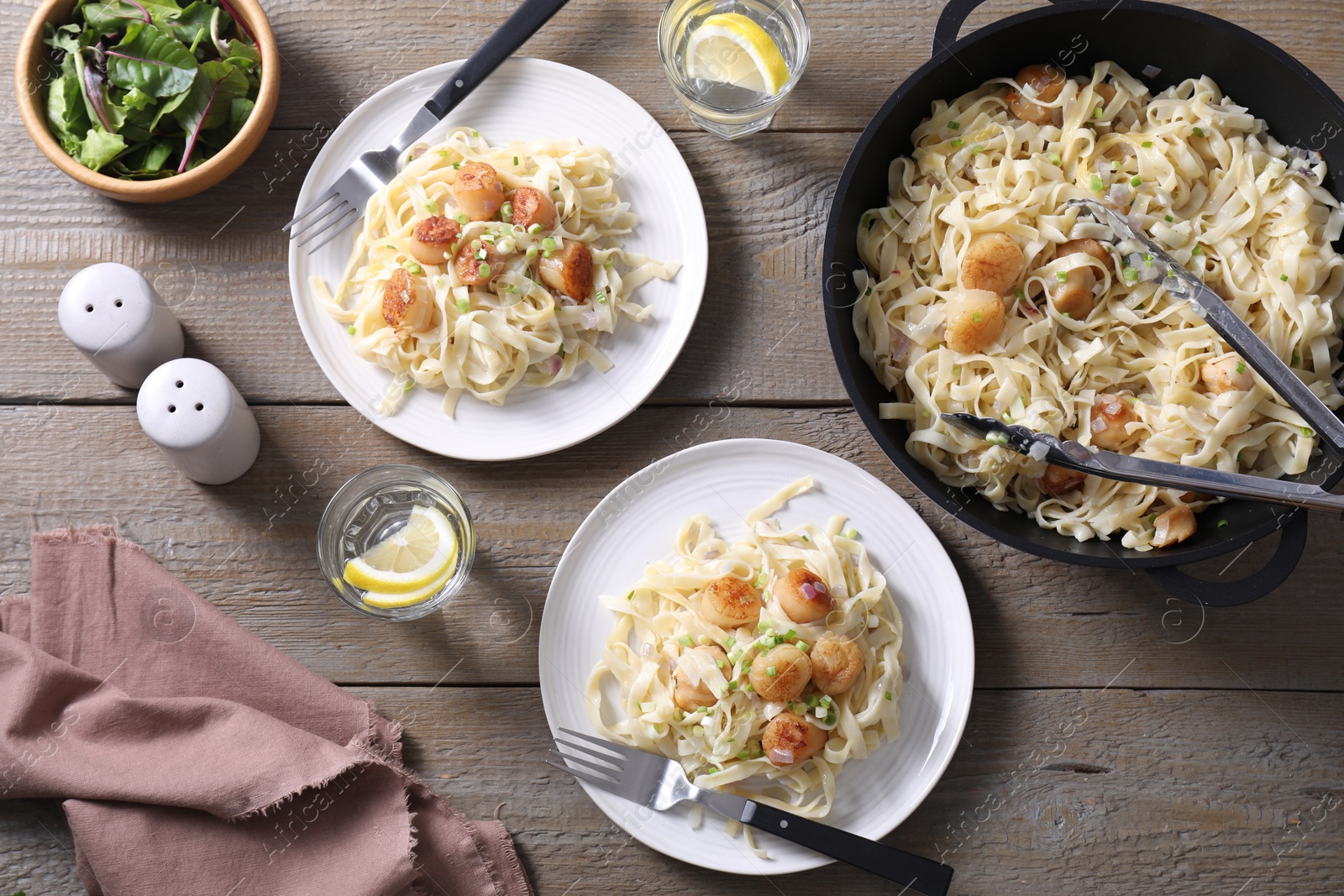 Photo of Delicious scallop pasta with onion served on wooden table, flat lay
