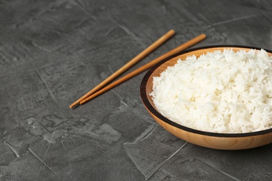 Photo of Bowl of boiled rice and chopsticks on grey table. Space for text