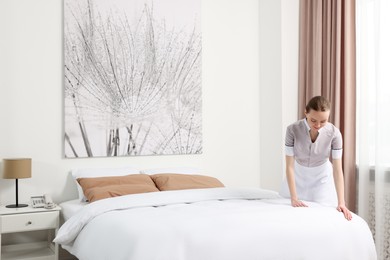 Young maid making bed in hotel room. Space for text