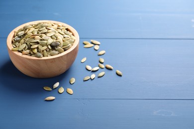 Photo of Bowl with peeled pumpkin seeds on blue wooden table. Space for text