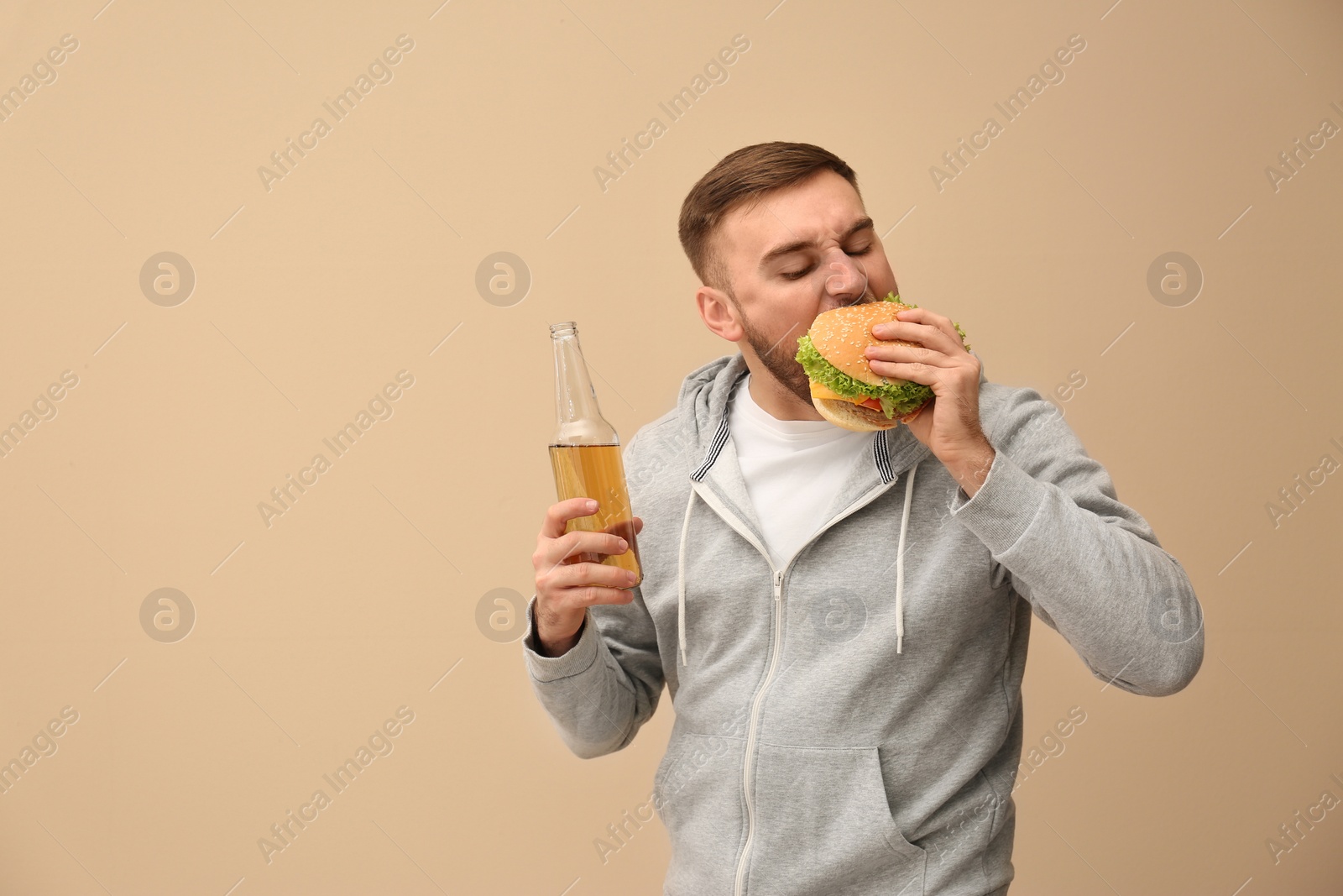 Photo of Young man with beer eating tasty burger on color background. Space for text
