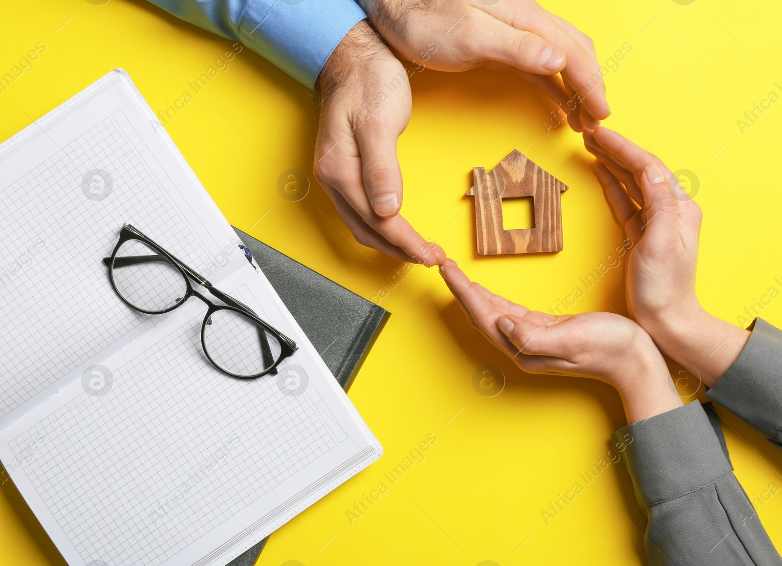 Photo of Couple holding hands near figure of house on color background, top view. Home insurance