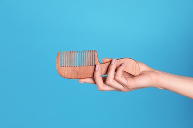 Photo of Woman holding wooden hair comb against blue background, closeup