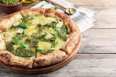 Photo of Delicious pizza with pesto, cheese and basil on wooden table. Space for text