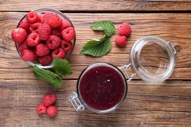 Jar of delicious raspberry jam, fresh berries and green leaves on wooden table, flat lay