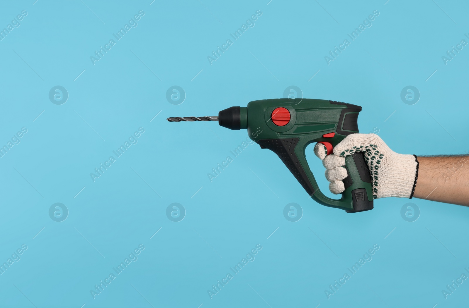 Photo of Worker in gloves with power drill on light blue background, closeup. Space for text