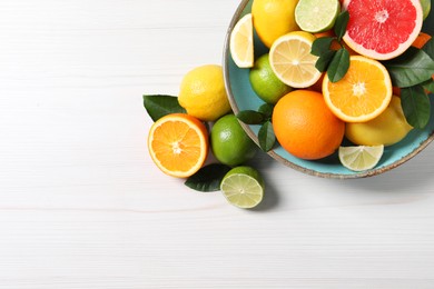 Photo of Different cut and whole citrus fruits on white wooden table, top view. Space for text