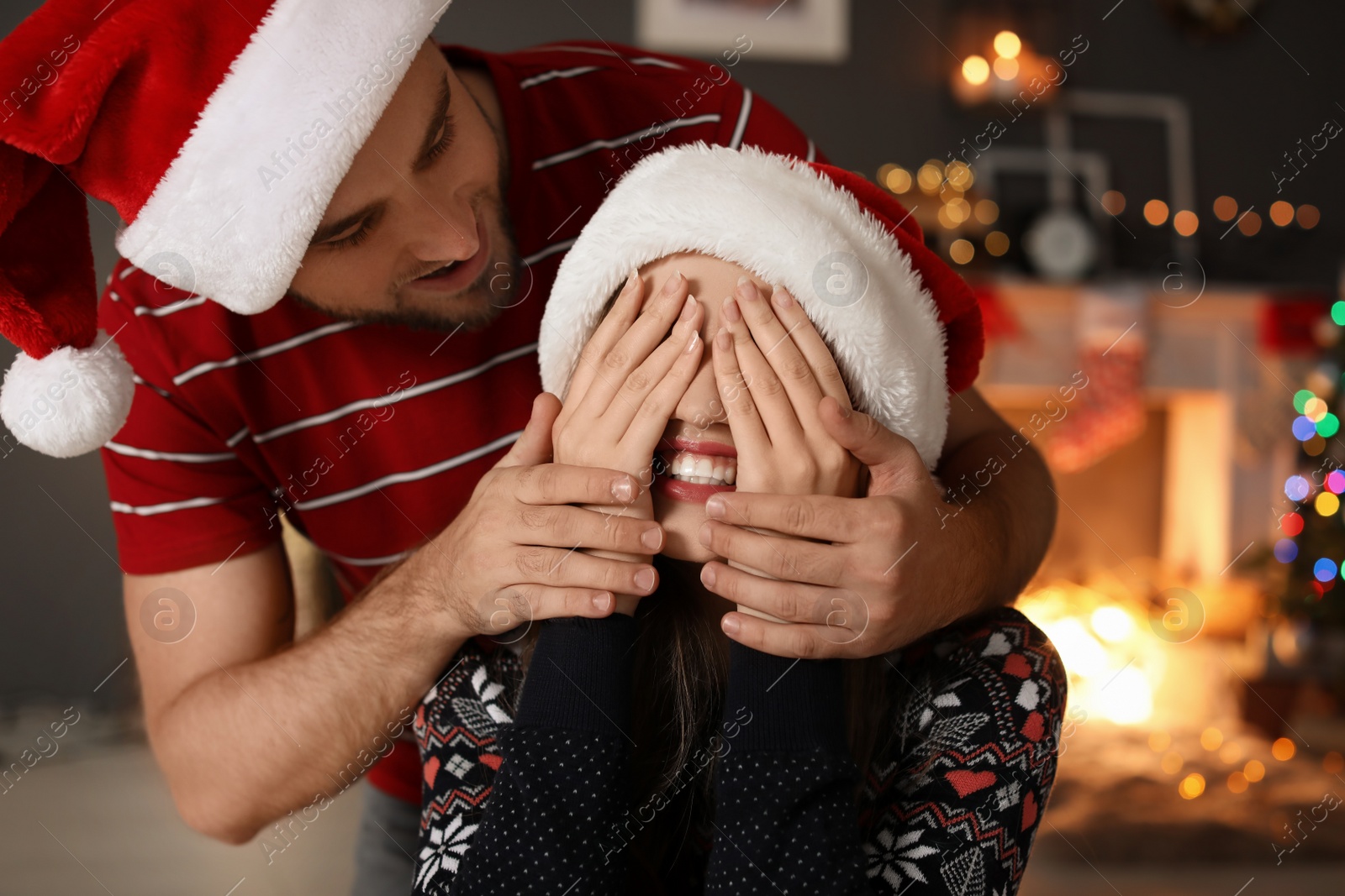 Photo of Happy young couple in Santa hats celebrating Christmas at home